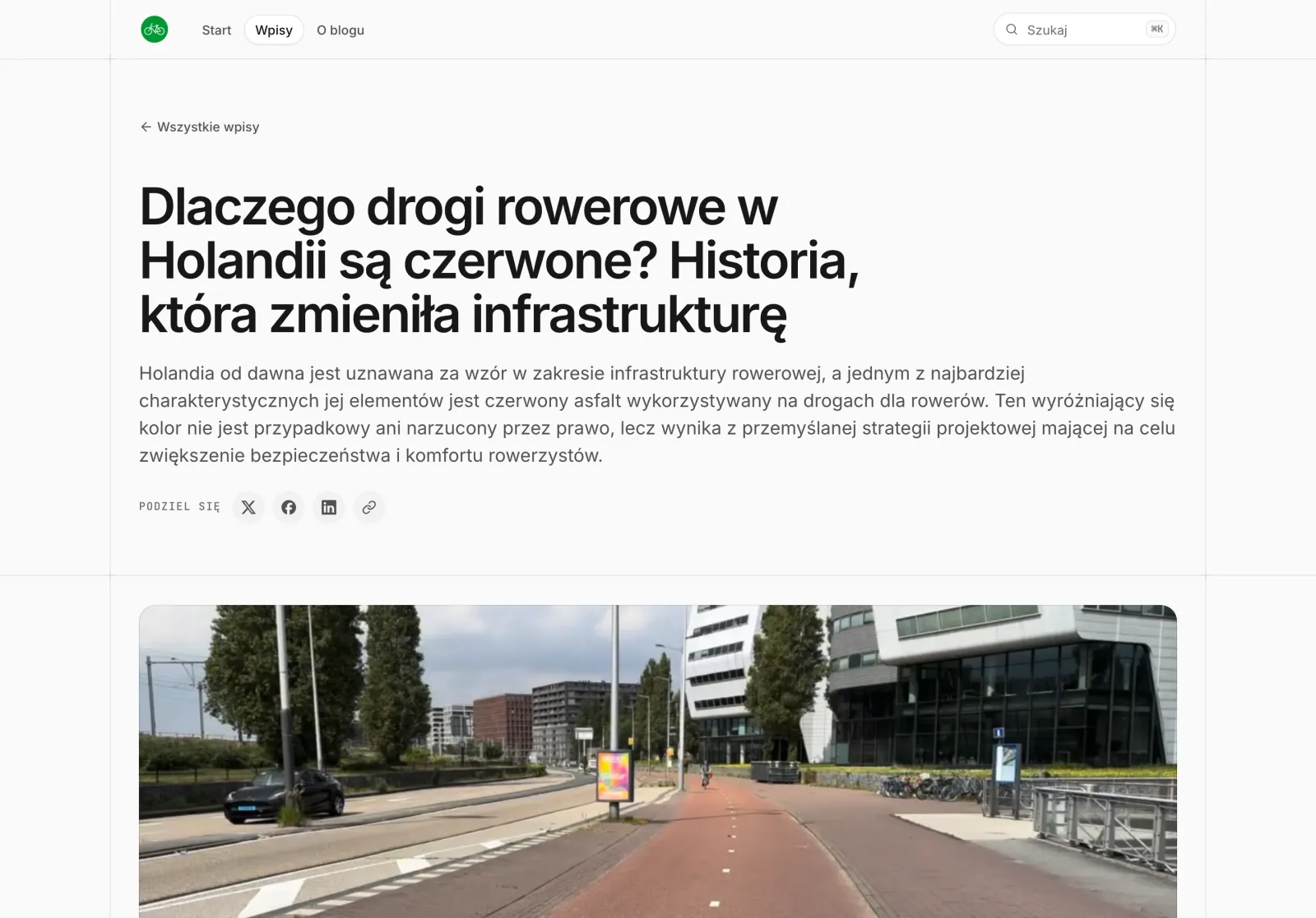 Nowy wpis „Dlaczego drogi rowerowe w Holandii są czerwone?”: tytuł i wstęp od razu pod menu, przyciski udostępniania i duże zdjęcie czerwonej drogi rowerowej.